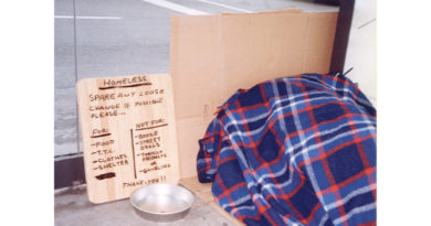 Photo of homeless person sleeping next to a cardboard sign
